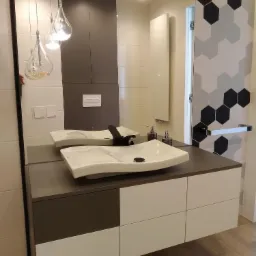 Nowoczesna łazienka z dwiema owalnymi umywalkami nablatowymi na szafce z szufladami w kolorze białym i szarym, lustro z widocznym grzejnikiem i heksagonalnymi płytkami na ścianie.