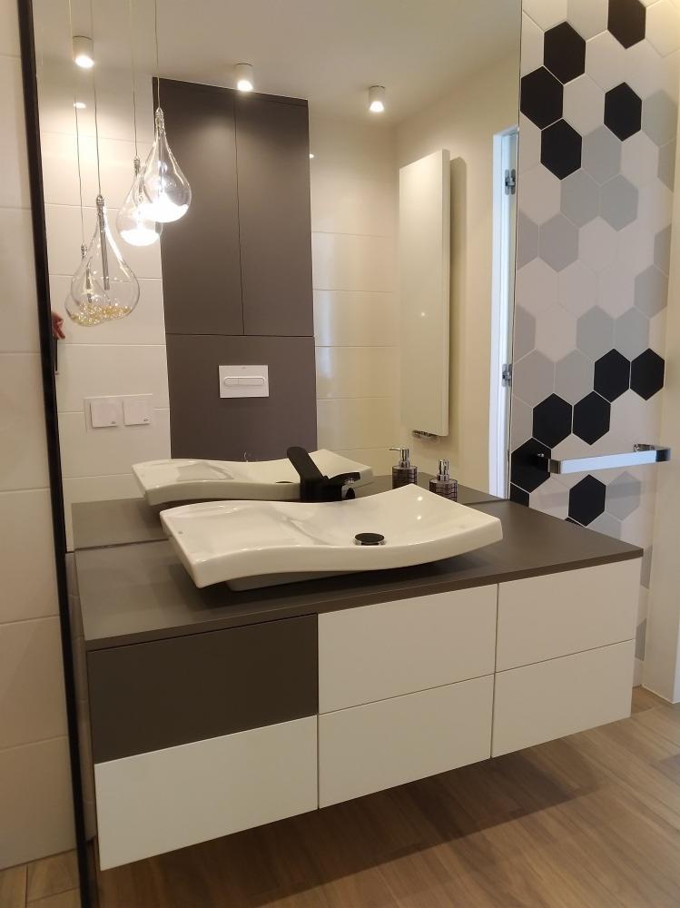 Nowoczesna łazienka z dwiema owalnymi umywalkami nablatowymi na szafce z szufladami w kolorze białym i szarym, lustro z widocznym grzejnikiem i heksagonalnymi płytkami na ścianie.