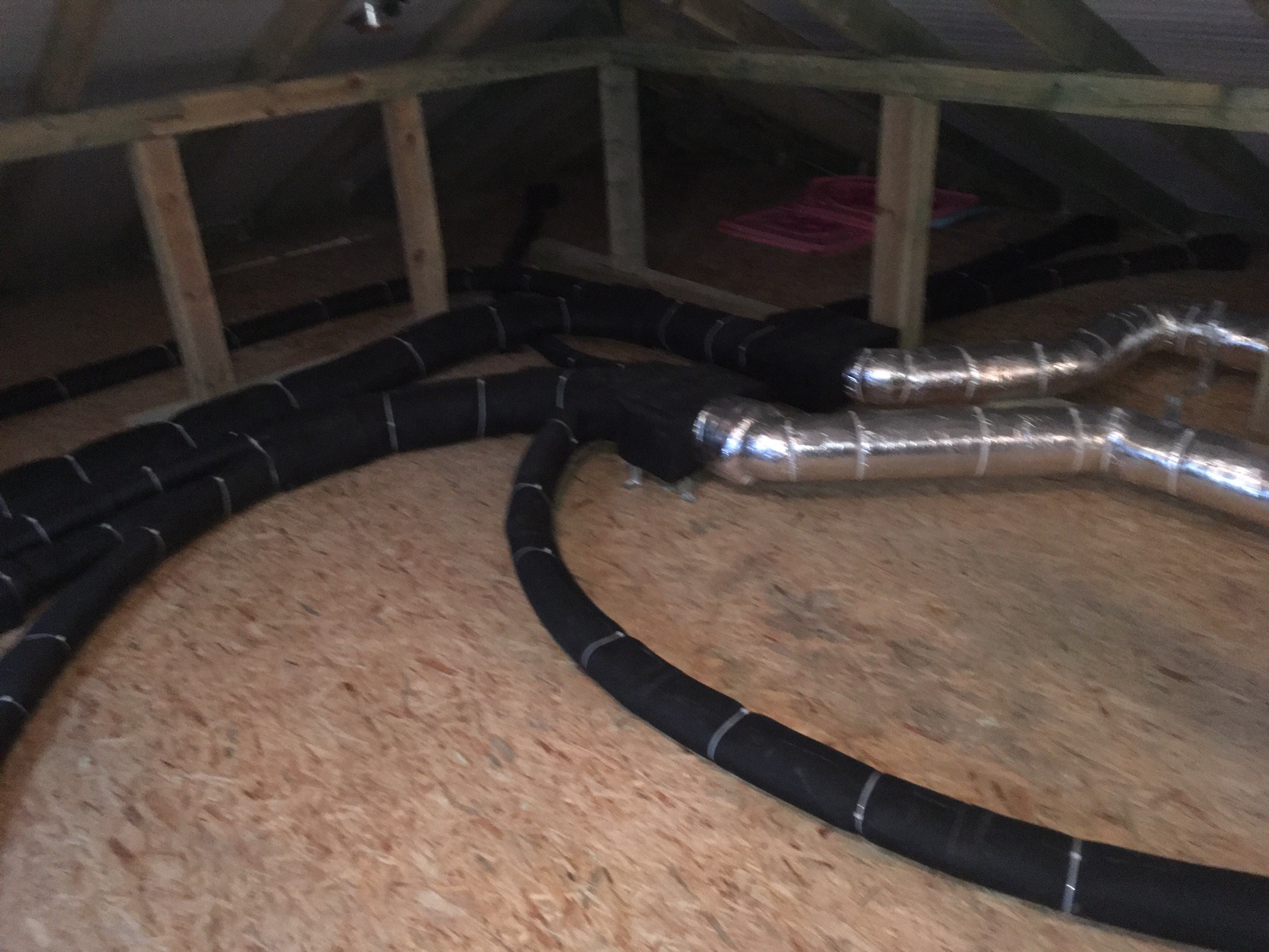 Czarno-srebrne, elastyczne przewody w izolacji, ułożone na drewnianej podłodze poddasza, widoczne elementy konstrukcji dachu.