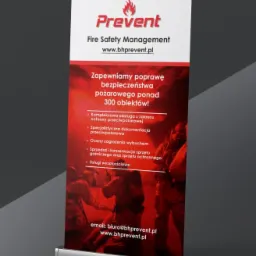 Roll-up reklamowy firmy Prevent Fire Safety Management z hasłem 'Zapewniamy poprawę bezpieczeństwa pożarowego ponad 300 obiektów!' oraz listą usług: kompleksowa obsługa, dokumentacja, oceny...
