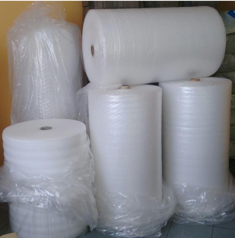 Stos rolek folii bąbelkowej różnej wielkości, część zapakowana w przezroczystą folię, ułożonych na podłodze.