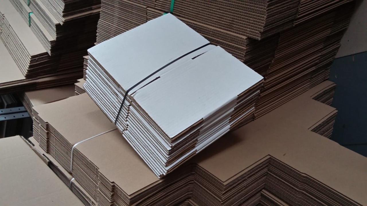 Stosy płaskich, niezłożonych pudełek kartonowych, część biała, część brązowa, spięte czarną gumką, przygotowane do użycia.