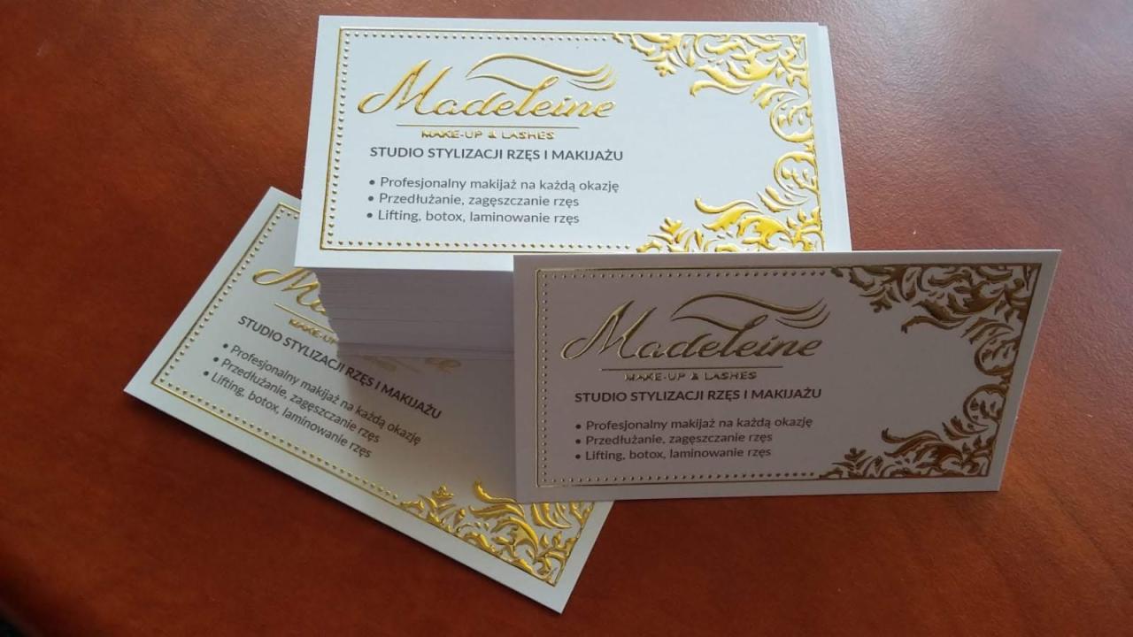 Stos wizytówek z tłoczonym złotym ornamentem i napisem 'Madeleine MAKE-UP & LASHES STUDIO STYLIZACJI RZĘS I MAKIJAŻU', prezentujących ofertę profesjonalnego makijażu, przedłużania i liftingu rzęs.