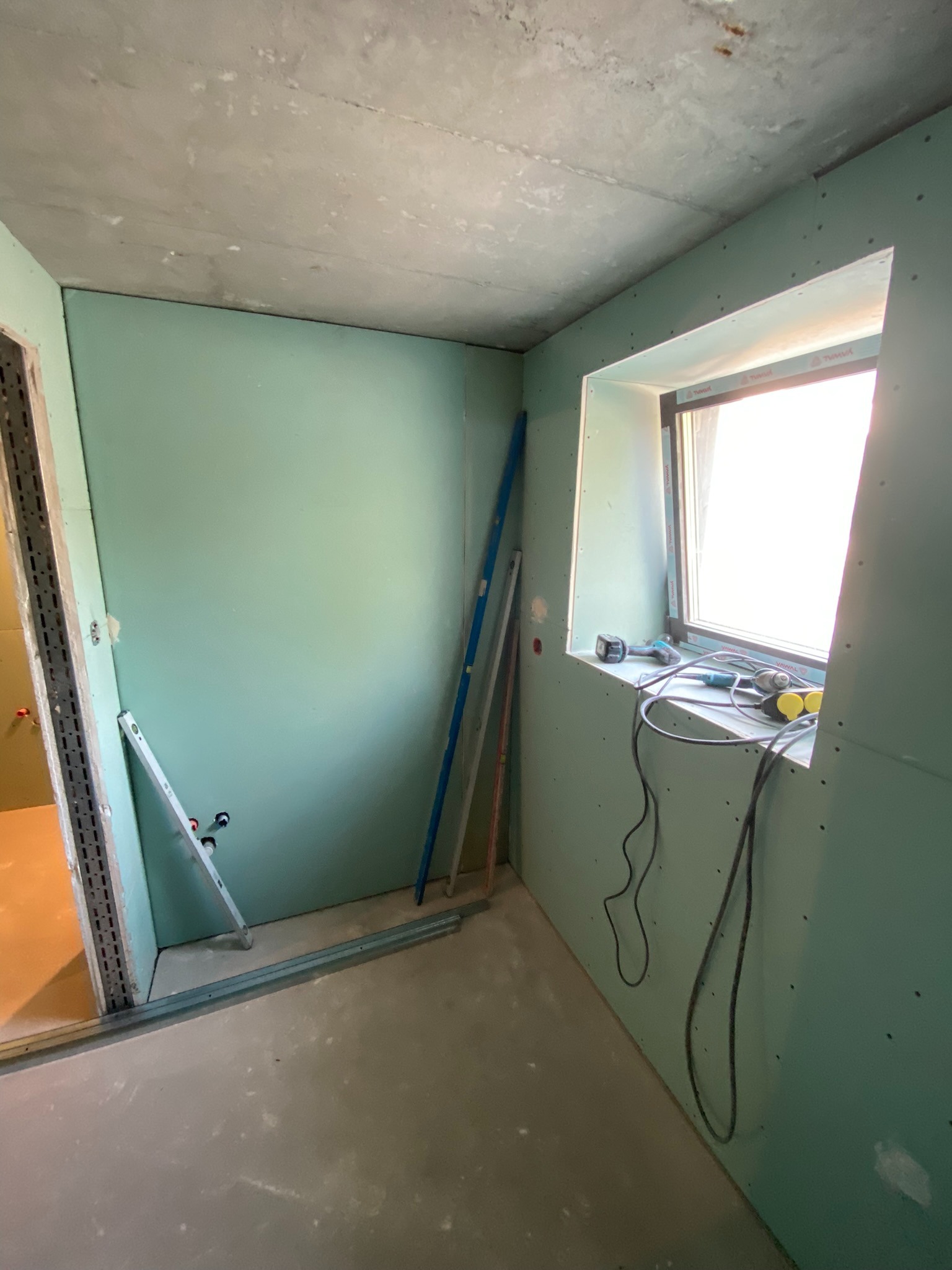 Montaż płyt gipsowo-kartonowych w Rytro, widoczne narzędzia pracy przy oknie i profile konstrukcyjne przy ścianach.