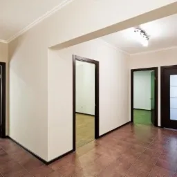 Korytarz po remoncie z trzema parami drzwi w ciemnych ramach, brązowe płytki podłogowe i białe ściany z listwami przysufitowymi.