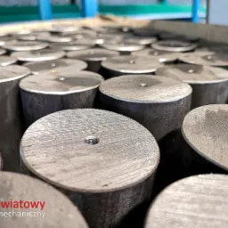 Seria metalowych cylindrów z gwintowanymi otworami na szczycie, ułożonych blisko siebie na metalowej powierzchni, z logo firmy w rogu.