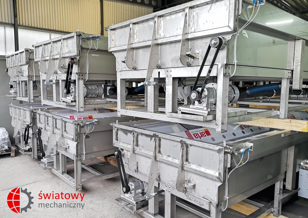 Rząd identycznych, stalowych maszyn przemysłowych z napędem pasowym, prawdopodobnie do obróbki lub sortowania, ustawionych w hali produkcyjnej.