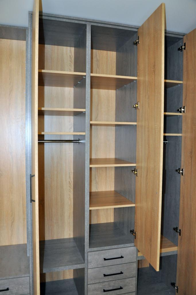 Wnętrze szafy z otwartymi drzwiami, widoczne półki i szuflady w szarym i drewnopodobnym wykończeniu, metalowy drążek na ubrania.