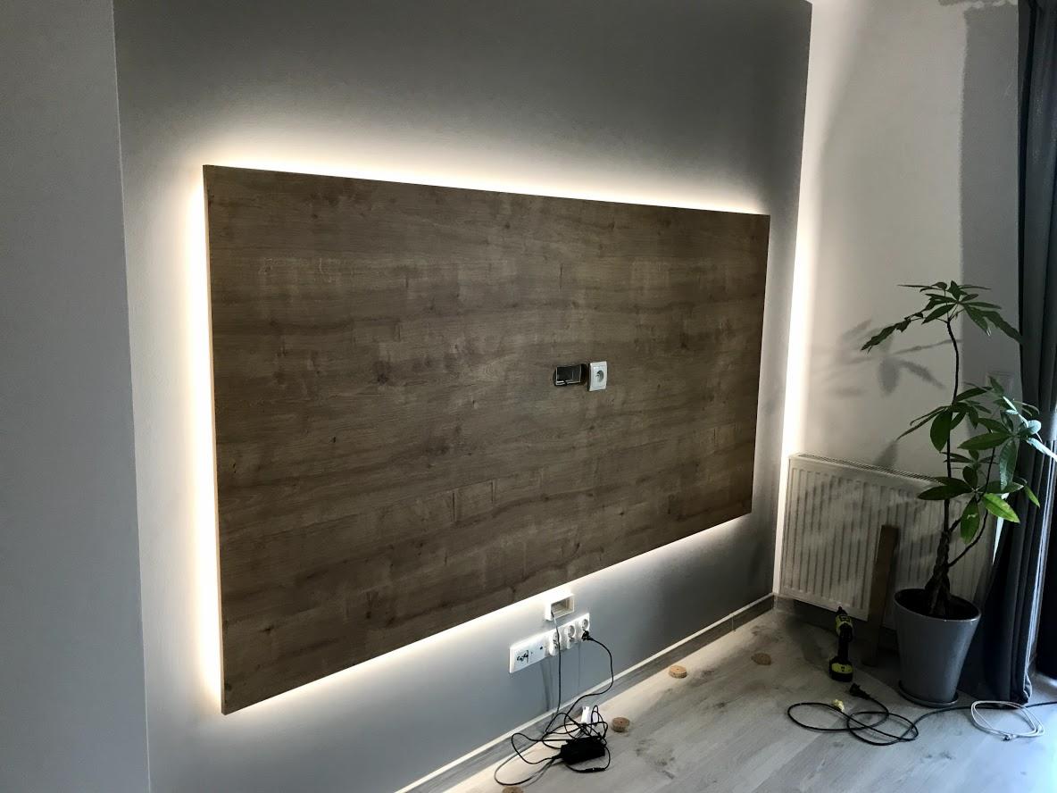 Panel ścienny z drewnopodobną okleiną, podświetlony taśmą LED, z widocznymi gniazdkami i osprzętem elektrycznym w trakcie montażu, narzędzia na podłodze.