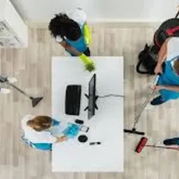 Ekipa sprzątająca w akcji, widok z góry: pracownicy w niebieskich uniformach i rękawicach czyszczą jasne biuro z drewnianą podłogą, używając odkurzaczy, ścierek i środków czystości. Na białym...