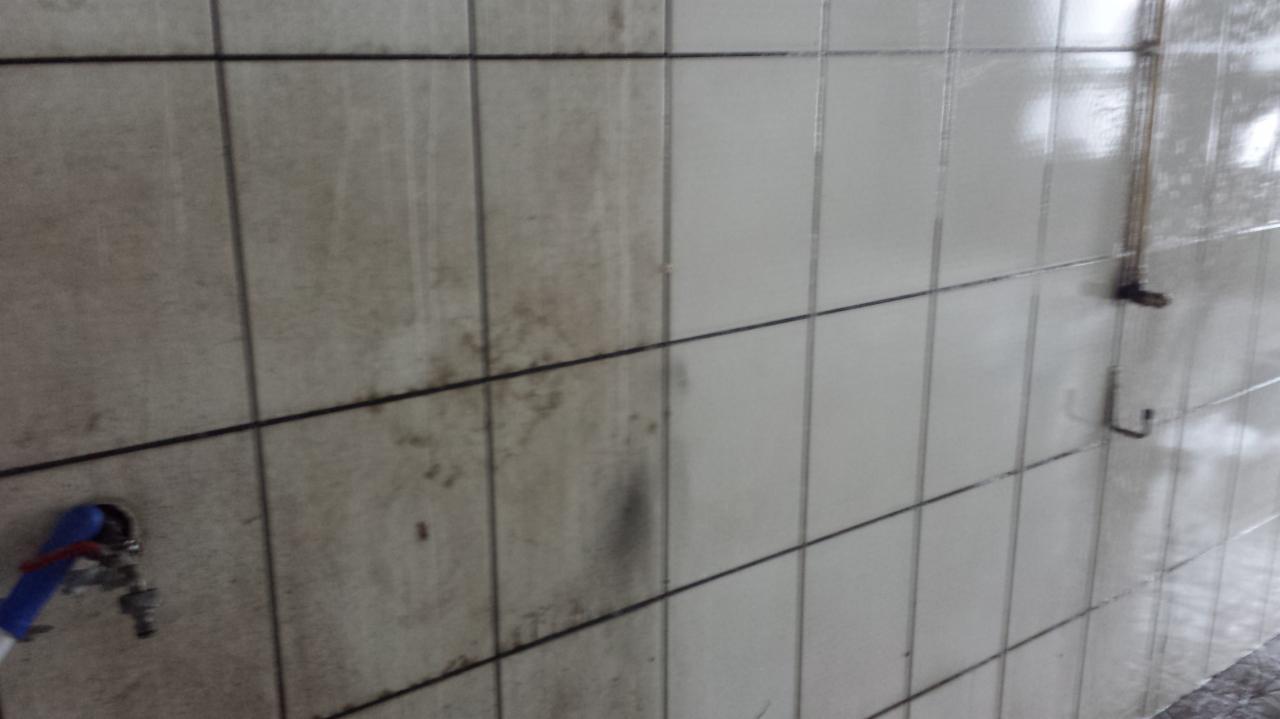 Kafelki ścienne częściowo wyczyszczone, widoczne różnice w czystości powierzchni, armatura z niebieskim uchwytem w lewym dolnym rogu.