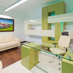 Nowoczesne biuro z zielonymi akcentami: szklane biurko z wyciętym wzorem, kremowa sofa pod obrazem z samochodami, designerska zabudowa ścienna z podświetleniem.