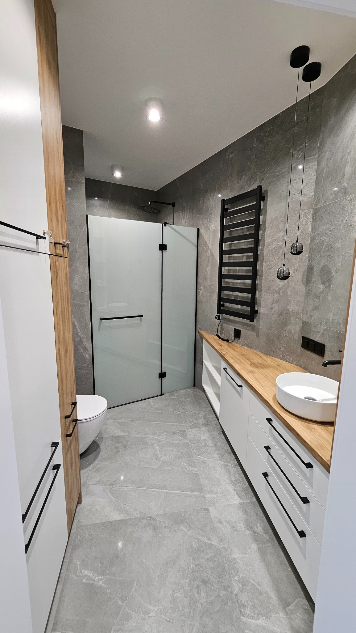 Nowoczesna łazienka w Jazowsku z szarymi płytkami imitującymi marmur, kabiną prysznicową walk-in i drewnianym blatem. Minimalistyczne oświetlenie.
