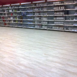 Jasna podłoga z paneli w sklepie z alkoholem, widok na regały z butelkami w tle.