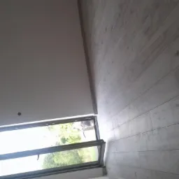 Nowoczesne okno dachowe uchylone, widok na zieleń z zewnątrz, jasna drewniana podłoga i białe ściany w wykończonym wnętrzu.