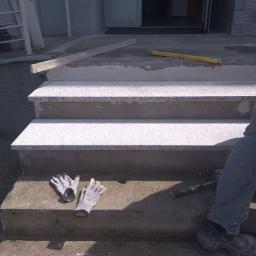 Glazurtech - Montaż granitowych płyt na schodach wejściowych, widoczne narzędzia pracy: poziomica, młotek i rękawice robocze.