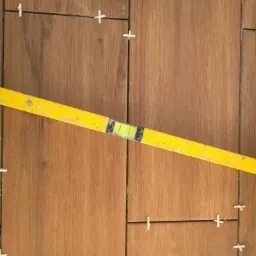 Układanie płytek imitujących drewno z użyciem poziomicy i krzyżyków dystansowych.