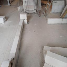 Glazurtech - Wznoszenie ścian z białych bloczków betonu komórkowego na podłodze w trakcie budowy lub remontu, widoczna drabina i narzędzia.