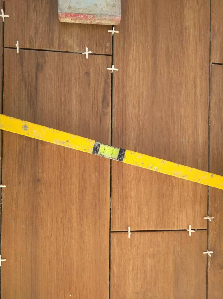 Układanie płytek imitujących drewno z użyciem poziomicy i krzyżyków dystansowych.