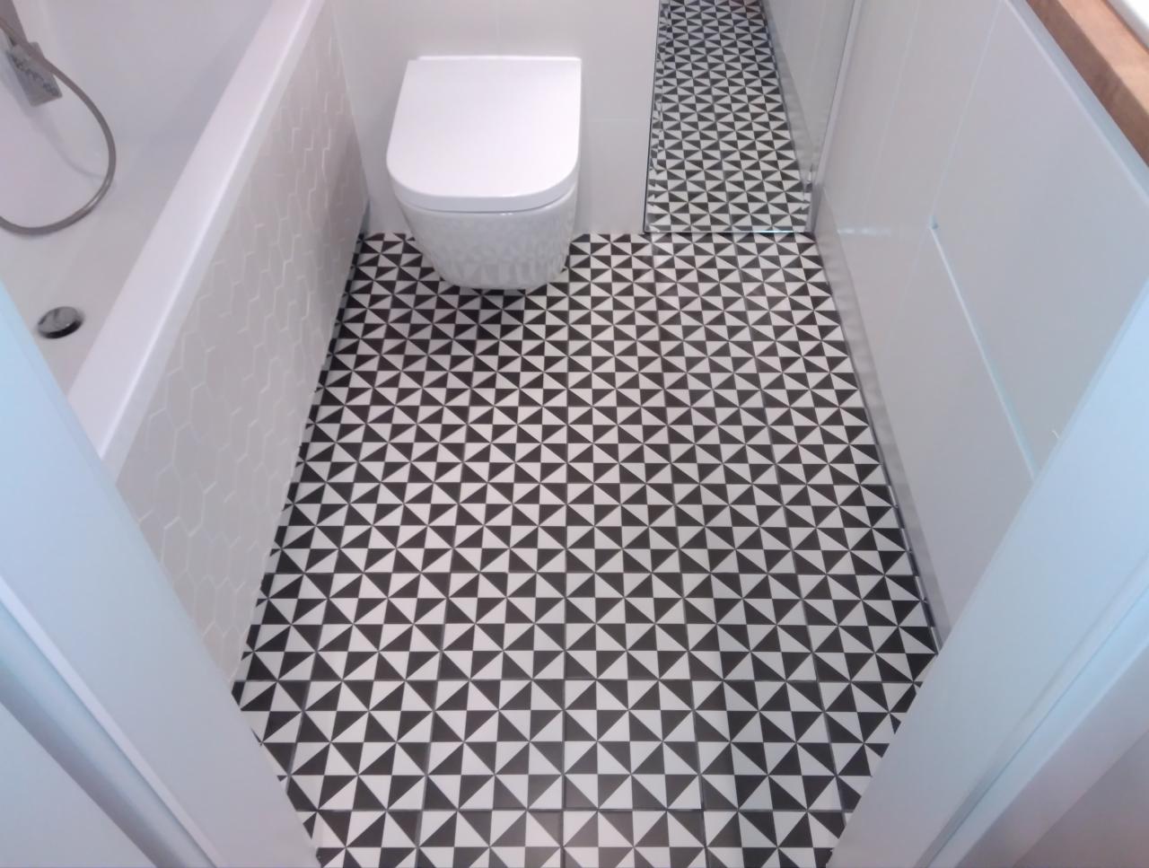 Biała toaleta kompaktowa i wanna z panelami w kształcie plastra miodu w łazience z podłogą wyłożoną czarno-białą mozaiką z trójkątów.