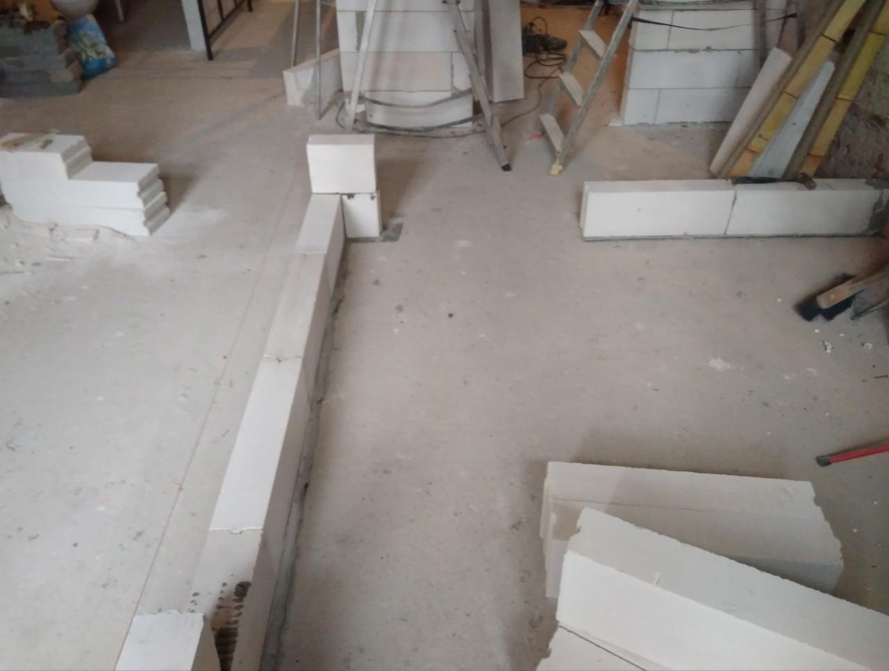 Wznoszenie ścian z białych bloczków betonu komórkowego na podłodze w trakcie budowy lub remontu, widoczna drabina i narzędzia.