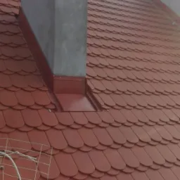 Czerwony dach z dachówki karpiówki, nowy komin obłożony blachą, widoczna antena telewizyjna.