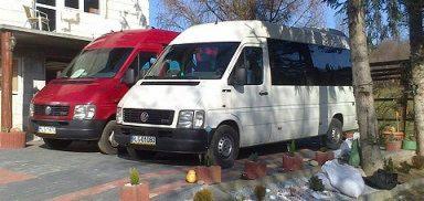 Dwa busy: czerwony i biały, zaparkowane obok budynku z widocznym numerem rejestracyjnym na białym busie.