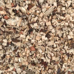 Jasnobrązowe zrębki drzewne z widocznymi fragmentami kory i struktury drewna, ułożone gęsto na płaskiej powierzchni.