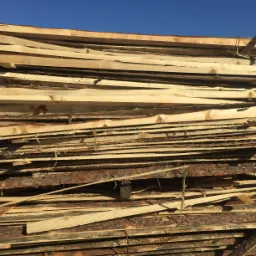 Stos świeżo przetartego drewna z widoczną korą, ułożonego warstwami pod błękitnym niebem.