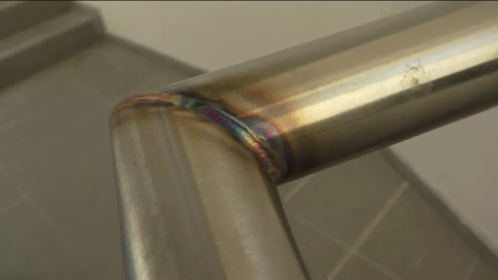 Precyzyjne złącze spawane dwóch rur ze stali nierdzewnej, widoczne charakterystyczne kolory dyfrakcyjne na spoinie.