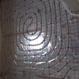 Montaż rur ogrzewania podłogowego na izolacji z siatką w Redzie, widoczne czarne uchwyty mocujące.