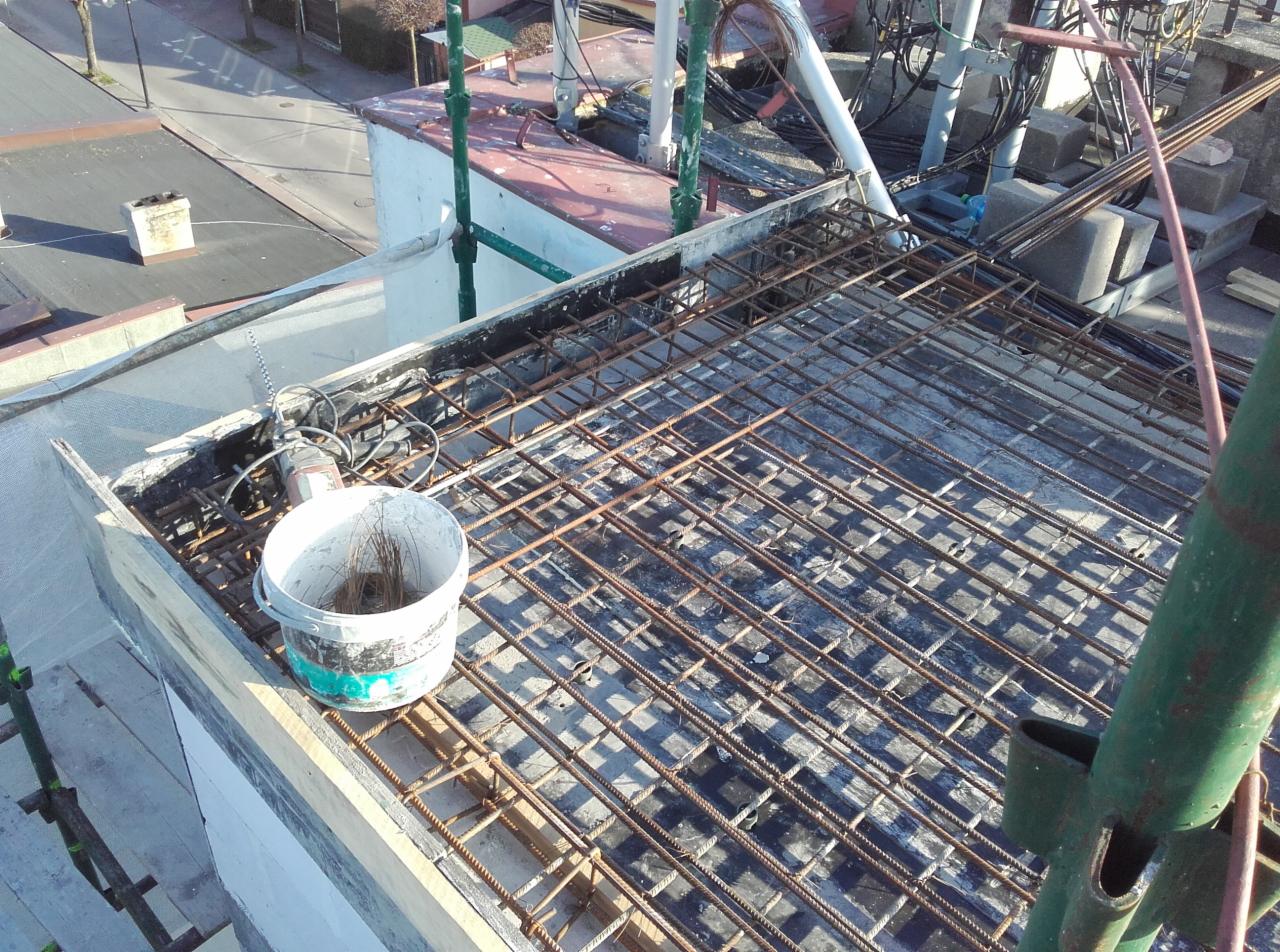 Zbrojenie stropu przygotowane do zalania betonem, widoczny wiadro z resztkami drutu wiązałkowego, szlifierka kątowa oraz elementy rusztowania.