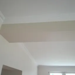 Pomieszczenie po malowaniu ścian i sufitu na biało, z widoczną listwą dekoracyjną pod sufitem i fragmentem lampy.