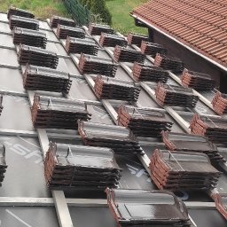 WORK IN WOOD Grzegorz Rachubiński - Przygotowane pakiety ceramicznej dachówki karpiówki ułożone rzędami na łatach i kontrłatach, gotowe do krycia dachu, widoczny fragment istniejącego dachu z dachówki ceramicznej.