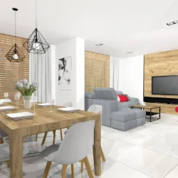 Jasne wnętrze z drewnianym stołem jadalnym, szarym narożnikiem i ścianą z okładziną imitującą drewno, oświetlone wiszącymi lampami o geometrycznych kloszach.