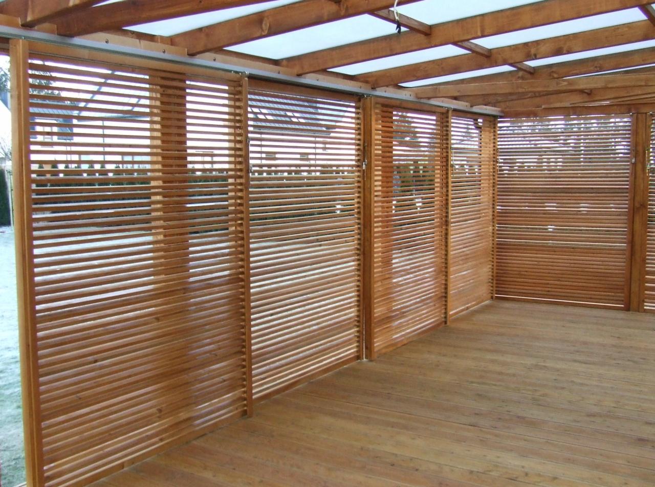 Zadaszona drewniana konstrukcja tarasowa z przesuwnymi panelami żaluzjowymi, zapewniającymi prywatność i ochronę przed słońcem, drewniana podłoga tarasowa, widok z wnętrza konstrukcji.