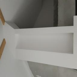 Zakład Remontowo Budowlany - Wnętrze w trakcie remontu, widoczna biała ściana z wnęką, fragment sufitu i drewniane elementy konstrukcyjne, surowe wykończenie.