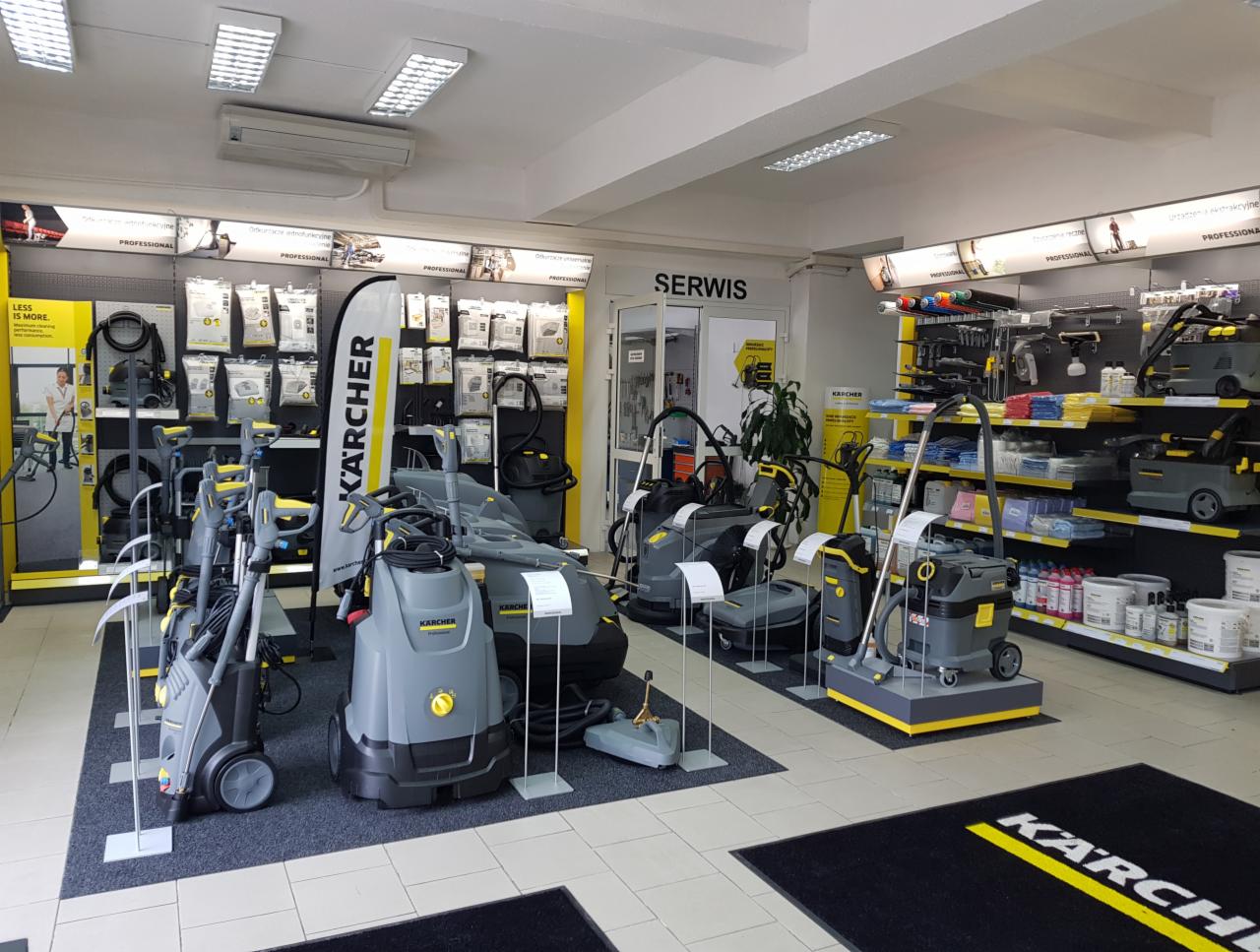 Ekspozycja w salonie firmowym Kärcher prezentująca różnorodne urządzenia czyszczące, w tym myjki ciśnieniowe i odkurzacze przemysłowe, ustawione na dywanikach z logo marki, z widocznym działem...