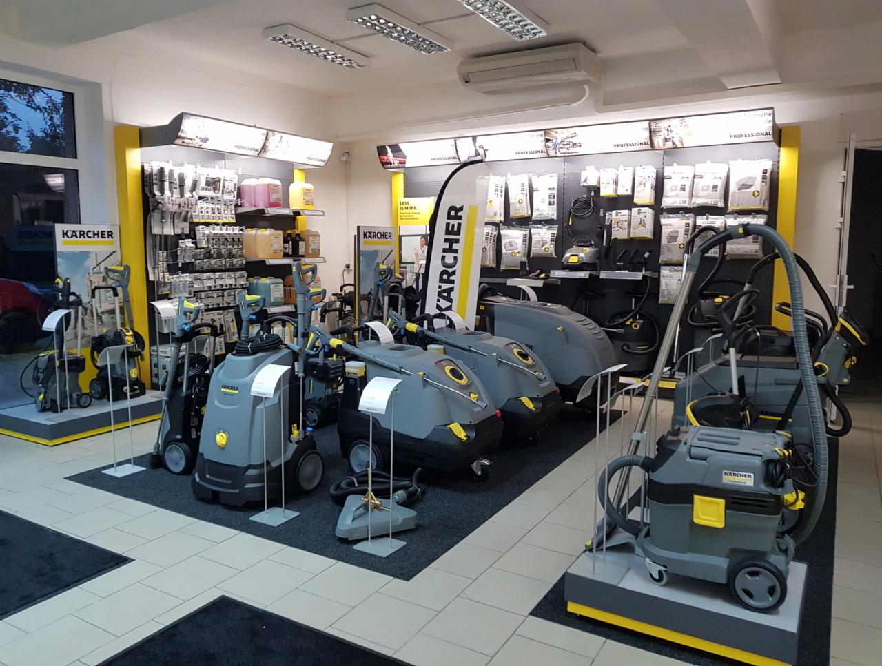 Ekspozycja w salonie Kärcher: szaro-żółte myjki ciśnieniowe i odkurzacze przemysłowe na czarnych dywanikach, z akcesoriami na półkach w tle.