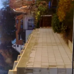 Wznoszenie ściany z bloczków betonu komórkowego Ytong, widoczne zbrojenie i zaprawa, w tle zabudowa jednorodzinna i drzewa, ujęcie w słoneczny dzień z dołu.