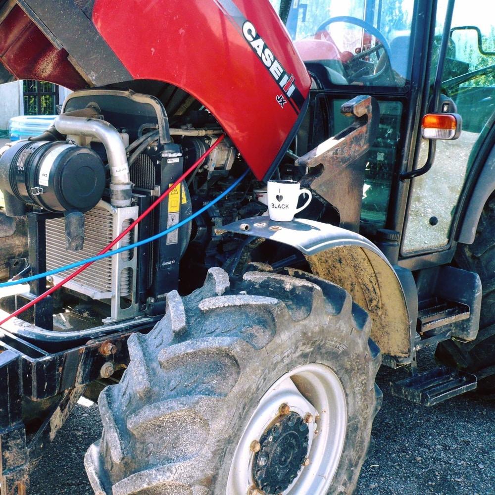 Otwarta maska ciągnika Case IH JX z widocznym silnikiem, chłodnicą i przewodami, na błotniku stoi kubek z napisem 'I love Black'.