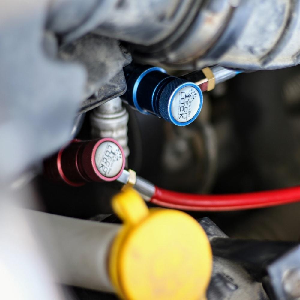 Podłączenie manometrów do zaworów niskiego i wysokiego ciśnienia układu chłodzenia pojazdu podczas serwisu, widoczny przewód czerwony i żółty korek zbiornika płynu.