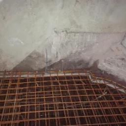 Przygotowanie zbrojenia pod wylewkę betonową w pomieszczeniu z surowymi ścianami, widoczny worek z zaprawą budowlaną w rogu.