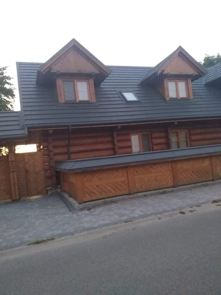 Dom z bali z ciemną, dachówką karpiówką i drewnianymi lukarnami, widok z dołu.