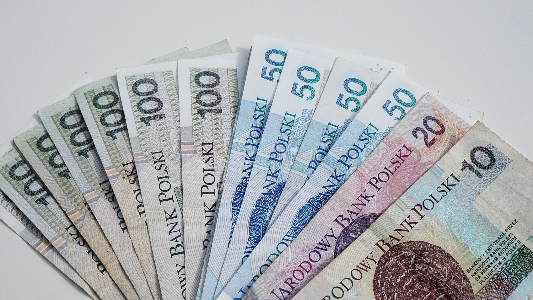 Rozłożony wachlarz polskich banknotów o nominałach 100, 50, 20 i 10 zł na białym tle, ukazujący różnorodność waluty krajowej.