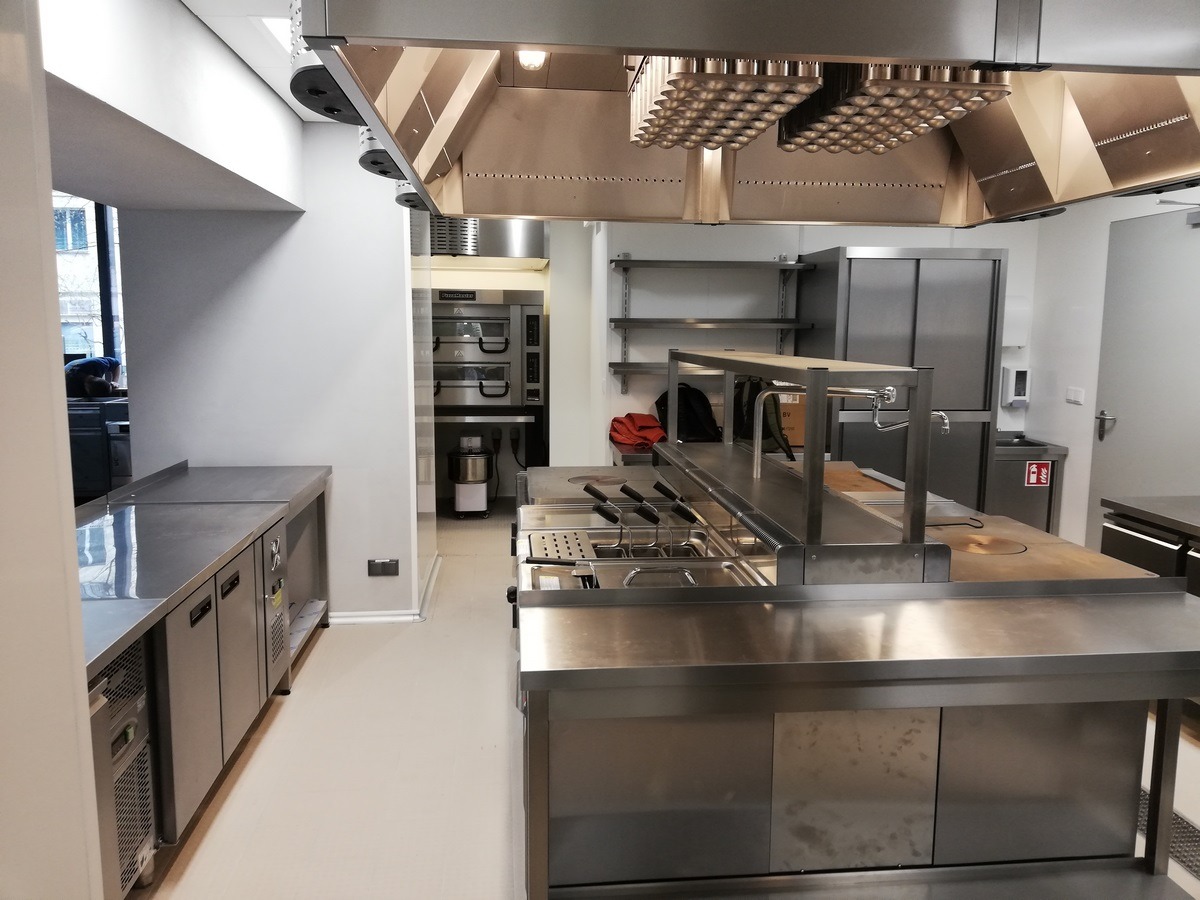 Profesjonalna kuchnia gastronomiczna ze stali nierdzewnej, z widocznym okapem z systemem kulek, piecem konwekcyjnym, stołami roboczymi i szafkami chłodniczymi.