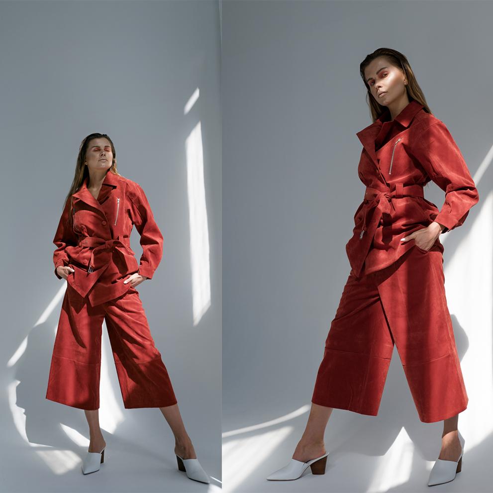 Dwa ujęcia modelki w rudym, zamszowym komplecie: spodniach culottes i wiązanej kurtce z suwakiem, na białym tle z plamami światła, w białych skórzanych czółenkach.