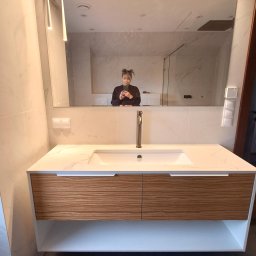 Maniak Design Anna Maniak - Nowoczesna łazienka z umywalką nablatową i szafką z drewnianymi frontami. W lustrze odbija się osoba robiąca zdjęcie telefonem. Widoczne oświetlenie LED nad lustrem i marmurowe płytki na ścianach.