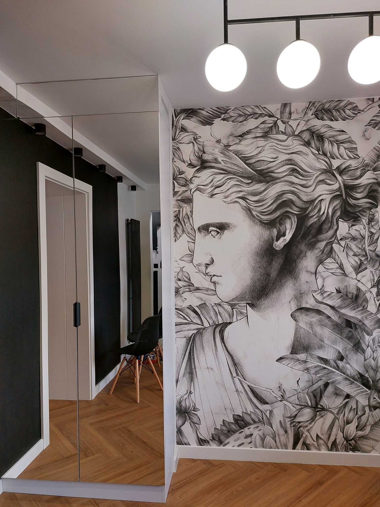 Nowoczesny przedpokój z lustrzaną szafą w zabudowie, parkietem ułożonym we wzór jodełki i tapetą z motywem grafiki przedstawiającej profil kobiety w otoczeniu liści.