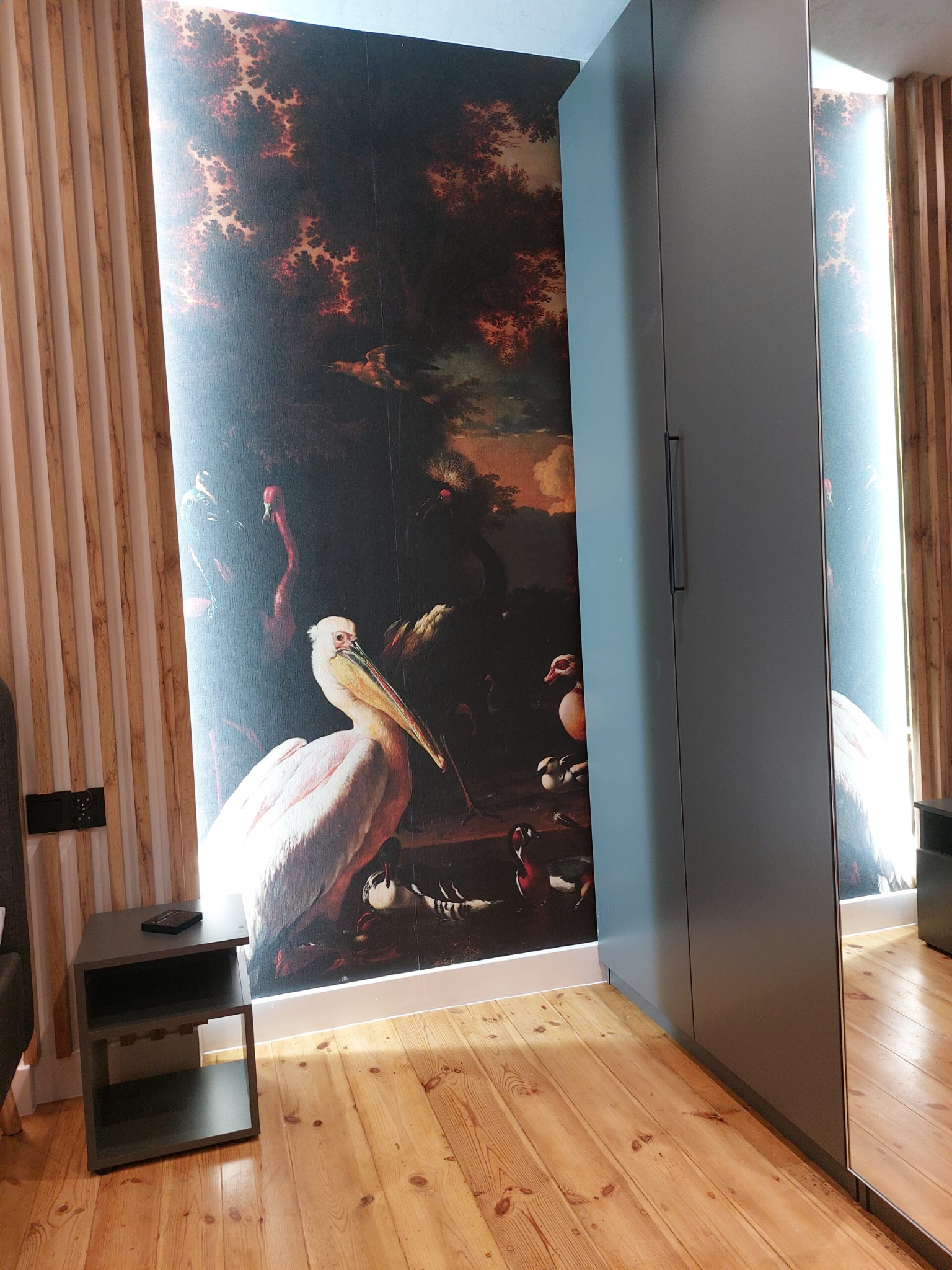 Pokój z fototapetą przedstawiającą ptaki w stylu starych mistrzów, drewnianą boazerią, szarą szafą i drewnianą podłogą, oświetlony światłem dziennym